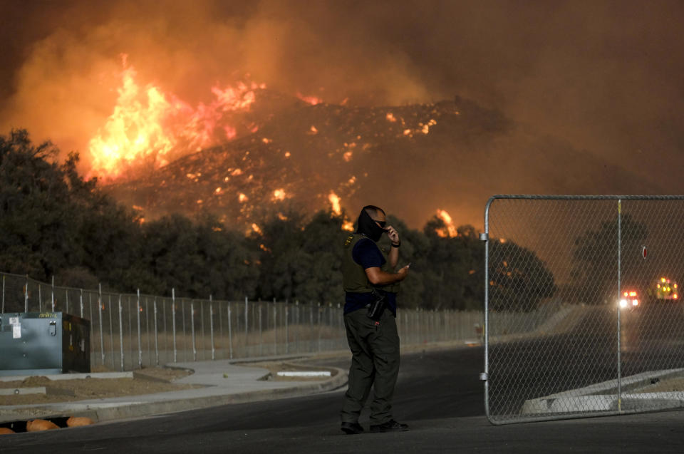 A sheriff's deputy stands guard at a gate near a hillside as the Holy Fire burns in the Cleveland National Forest at Temescal Valley in Corona, Calif., Thursday, Aug. 9, 2018. (AP Photo/Ringo H.W. Chiu)