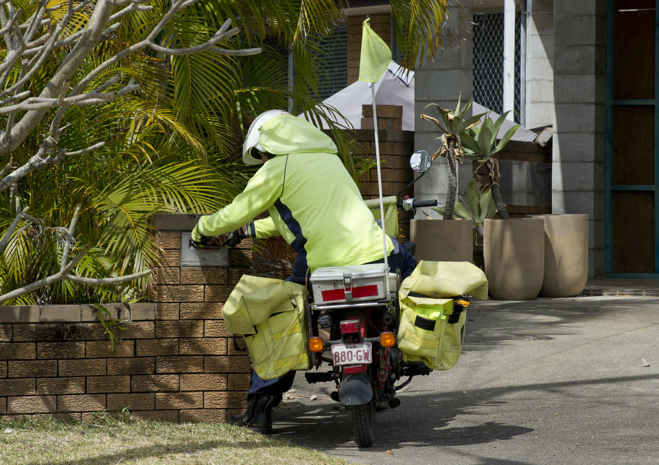 An Australia Post employee is seen delivering mail on a residential street on the Gold Coast.