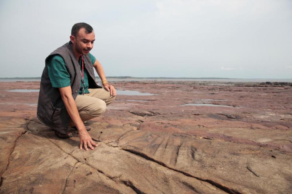 Archaeologist Jaime de Santana surveys ancient tool sharpening marks on Amazon river rock exposed by falling water level during drought in Manaus.