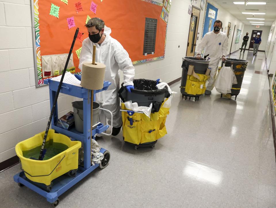 FILE - In this Nov. 5, 2020, file photo, Mike Wagner, left, and Ken Gleich, dressed in hazmat suits, wheel cleaning carts to their next classroom as they disinfect Richard A. Simpson Elementary School in Arnold, Mo. A deadly rise in COVID-19 infections is forcing state and local officials to adjust their blueprints for fighting a virus that is threatening to overwhelm health care systems. Schools are scrapping plans to reopen classrooms. More states are adopting mask mandates. (Colter Peterson/St. Louis Post-Dispatch via AP, File)