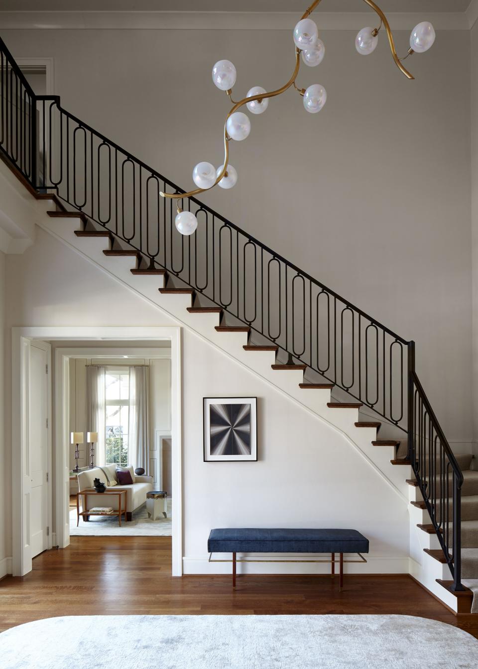 The home’s central staircase, which features new iron railing chosen by Liss, features a Harvey Probber bench in mahogany and brass, set under a Mark Gortjahn drawing, purchased at Pettit Art Partners. The striking ceiling light is a custom piece by Jeff Zimmerman from R & Company.