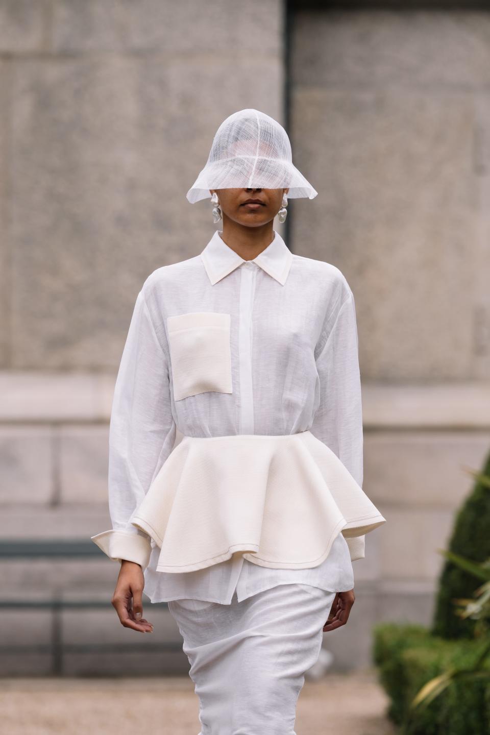 Model at the Mark Kenly Domino Tan wearing a white peplum outfit and bucket hat covering the eyes