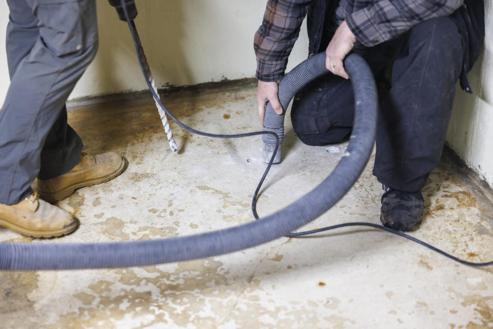 A close up of two workers using tools to detect a water leak underground.