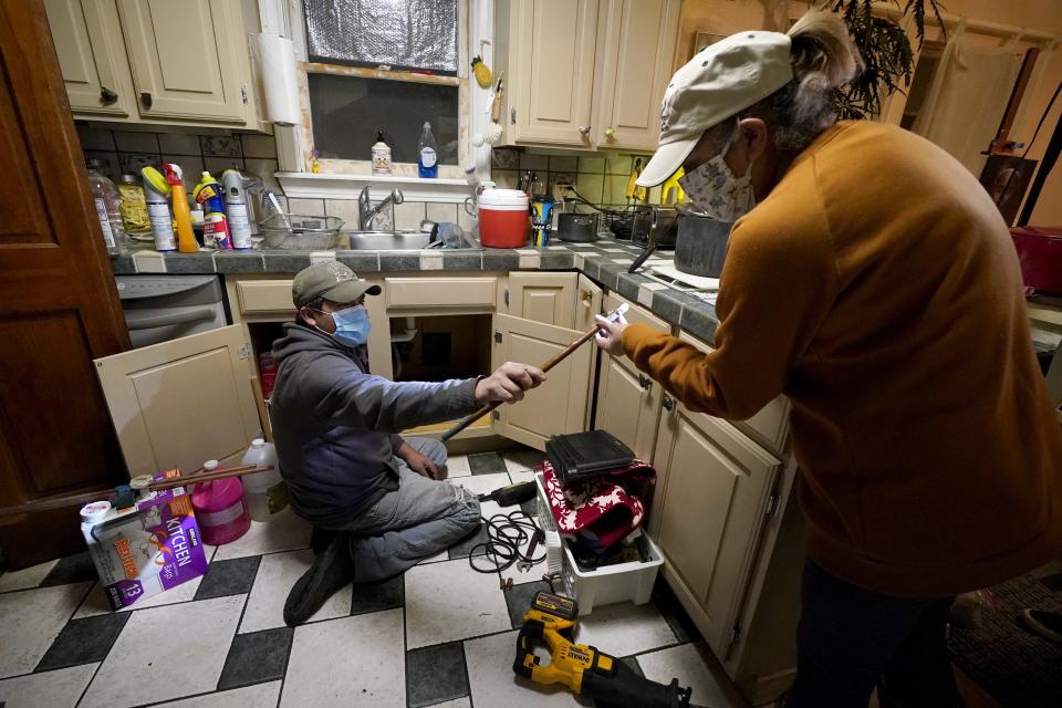 CORRECTS SPELLING OF LAST NAME TO VALERIO, NOT VALERIA - Handyman Roberto Valerio, left, hands homeowner Nora Espinoza the broken pipe after removing it from beneath her kitchen sink on Saturday, Feb. 20, 2021, in Dallas. The pipe broke during freezing temperatures brought by last week's winter weather. (AP Photo/Tony Gutierrez)