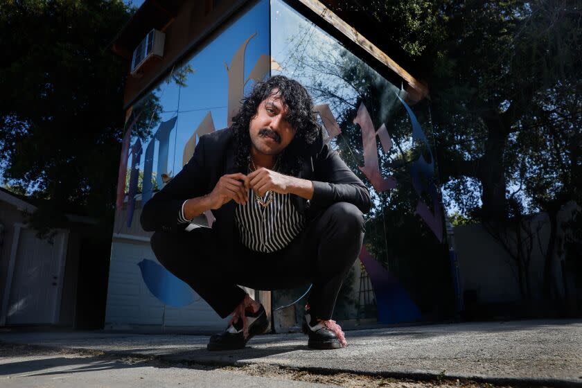 DJ Escuby (Enrique Tena Padilla), in a black suit and saddle shoes with pink laces, squats before a mirrored cube