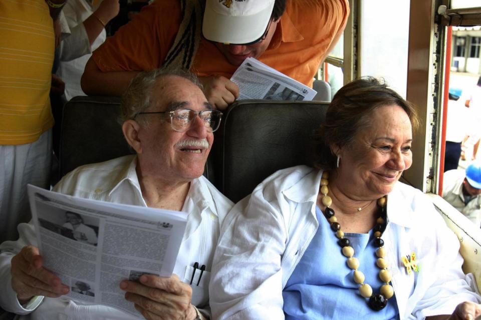 Gabriel Garcia Marquez sits in a train carriage alongside his wife as she smiles and looks out the window.