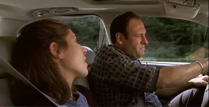 Jamie-Lynn Sigler and James Gandolfini in a car, both wearing seat belts. Jamie-Lynn looks to the side while James focuses on driving