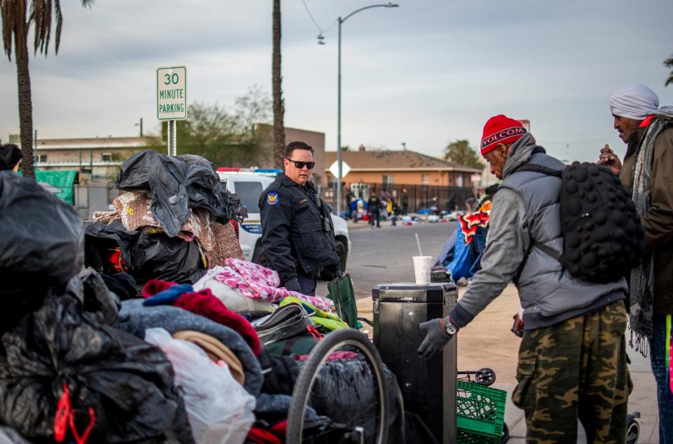 A Phoenix police officer tells people they have to move their stuff out of the way again during a clean-up of an encampment of around 400 people near Central Arizona Shelter Services and other services in Phoenix on Wednesday, Feb. 5, 2020.
