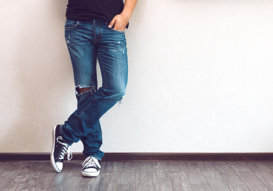 Young fashion man's legs in jeans and sneakers on wooden floor