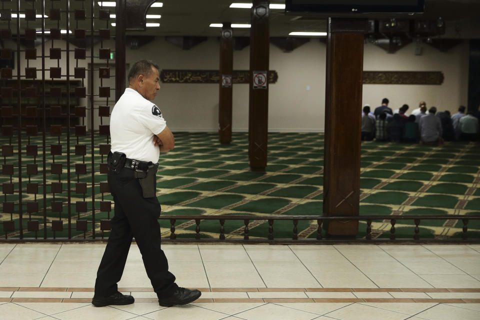 In this Friday, Oct. 2, 2018, photo armed security guard Mario Diaz walks across the hallway as a group of Muslims pray at Islamic Center of Southern California in Los Angeles. Diaz is one of two guards working at the mosque, one inside and the other one outside. Synagogues, mosques, churches and other houses of worship are routinely at risk of attack in many parts of the world. And so worshippers themselves often feel the need for visible, tangible protection even as they seek the divine. (AP Photo/Jae C. Hong)