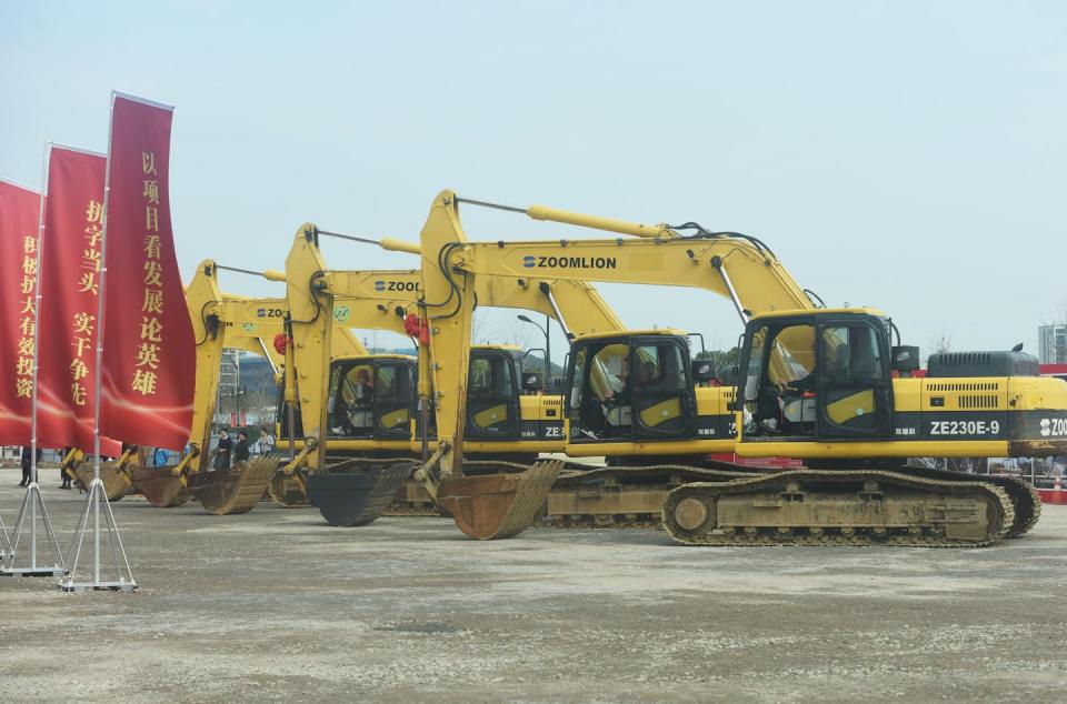 multiple yellow diggers positioned next to red flags with Chinese letters