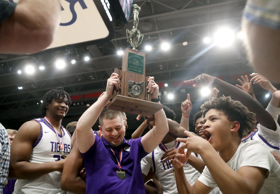 1. Pickerington Central boys basketball coach Eric Krueger hoists the Division I state championship trophy as his players celebrate a 55-48 win over Centerville on March 20 at the University of Dayton.