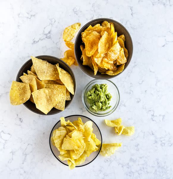 variety of chips in bowls on white, marble background