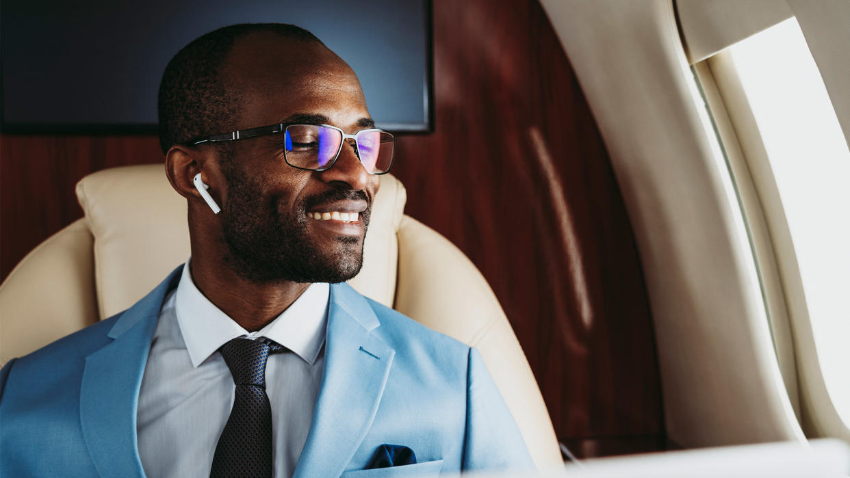  A man looks out the window of a plan while wearing AirPods. 