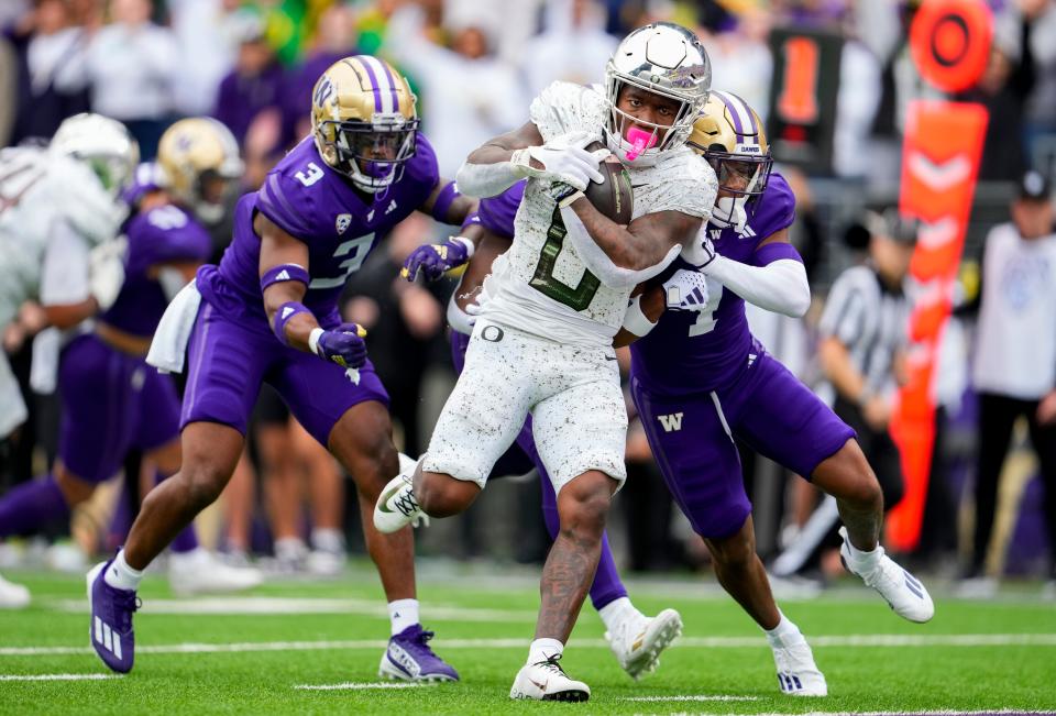 Oregon running back Bucky Irving runs for a touchdown through the tackle of Washington safety Mishael Powell (3) and cornerback Jabbar Muhammad (1) during the first half at Alaska Airlines Field at Husky Stadium.