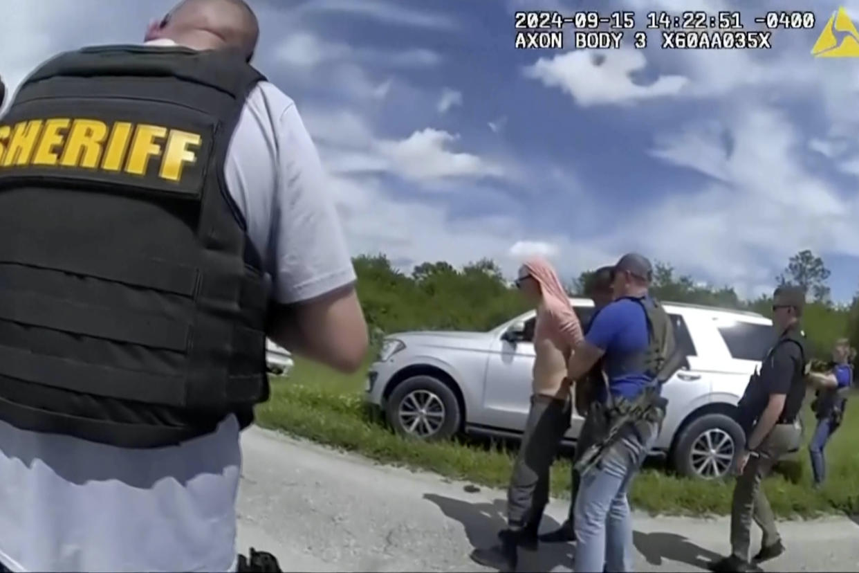 An image from police bodycam footage shows law enforcement officers arresting Ryan Routh along a highway in Florida.