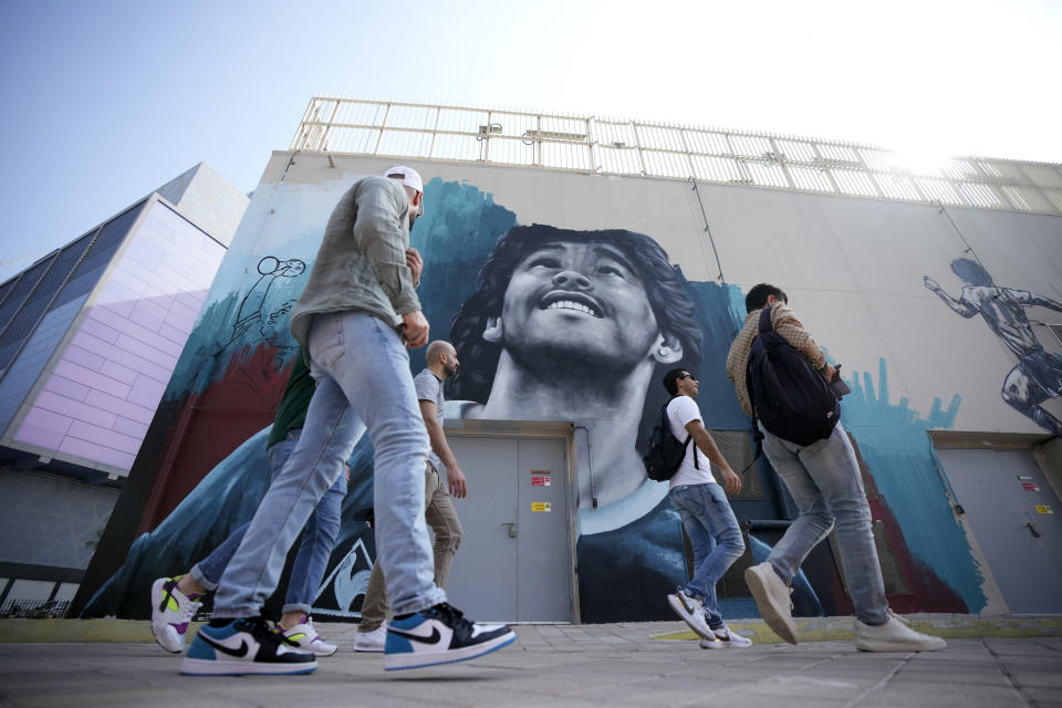 People walk past a mural of former Argentine player Diego Maradona, who led his country to the 1986 World Cup title, on a street prior to kick off the Qatar 2022 FIFA World Cup in Doha, Sunday, Nov. 20, 2022. (AP Photo/Eugene Hoshiko)