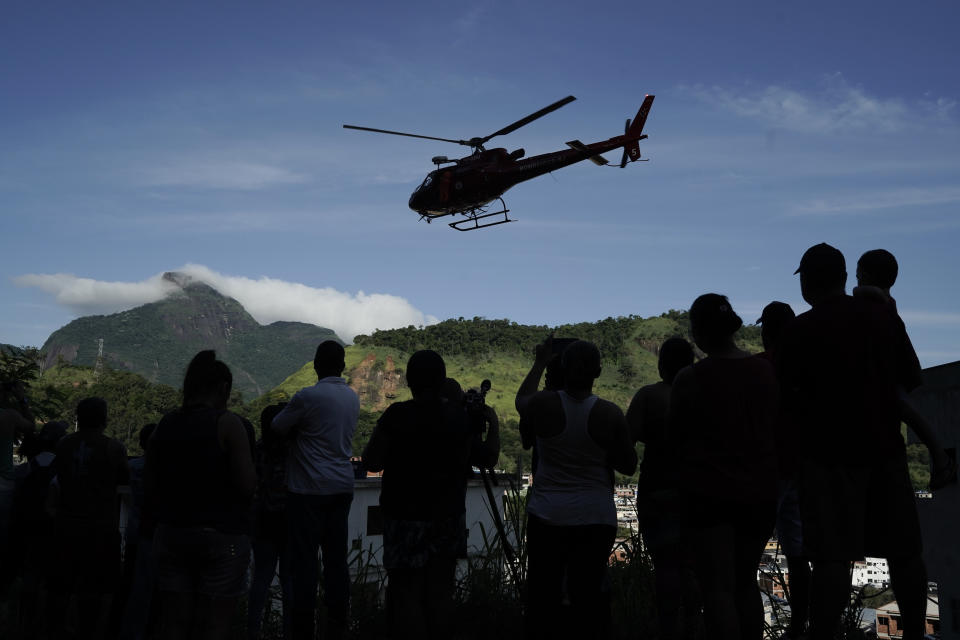 Residents watch a helicopter fly past transporting an injured person who was rescued from the rubble of two buildings that collapsed in the Muzema neighborhood, in Rio de Janeiro, Brazil, Friday, April 12, 2019. The collapse came in a western part of the city that was particularly hard hit by heavy rains this week that caused massive flooding. (AP Photo/Leo Correa)