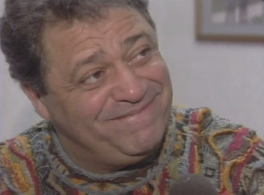 Wayne Fontes smiles while looking off-camera in a sweater full of different colors and patterns.