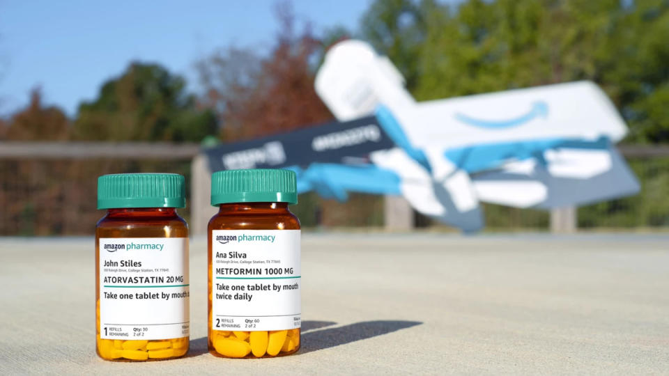 Photo marketing Amazon de deux flacons de pilules sur ordonnance posés sur une aire d'atterrissage extérieure.  Un drone Prime Air se trouve en arrière-plan (flou) devant des arbres.