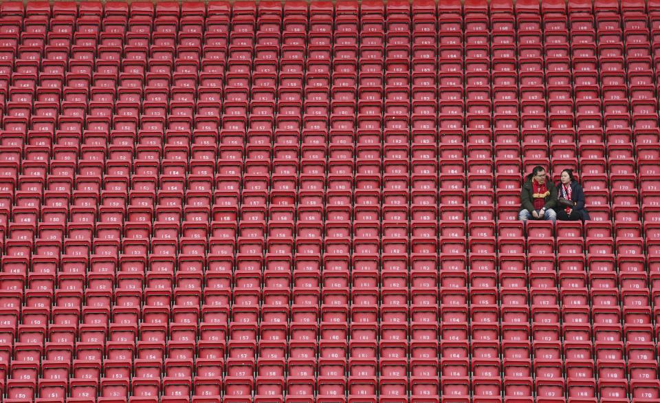 FILE - In this March 7, 2020, file photo, people sit surrounded by empty seats as they wait for the start of the English Premier League soccer match between Liverpool and Bournemouth at Anfield stadium in Liverpool, England. The crippling grip the coronavirus pandemic has had on the sports world has forced universities, leagues and franchises to evaluate how they might someday welcome back fans. (AP Photo/Jon Super, File)