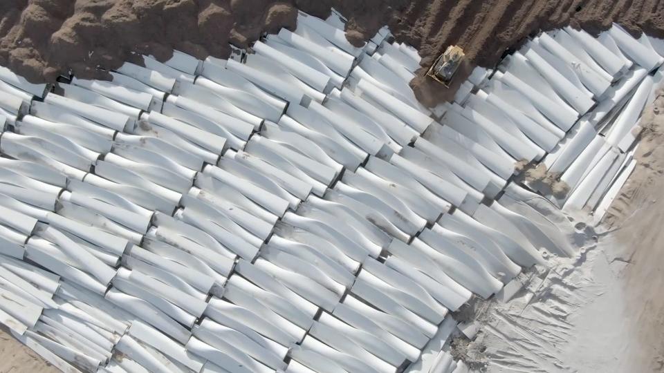 Six rows of white wind turbine blades neatly stacked on the ground.