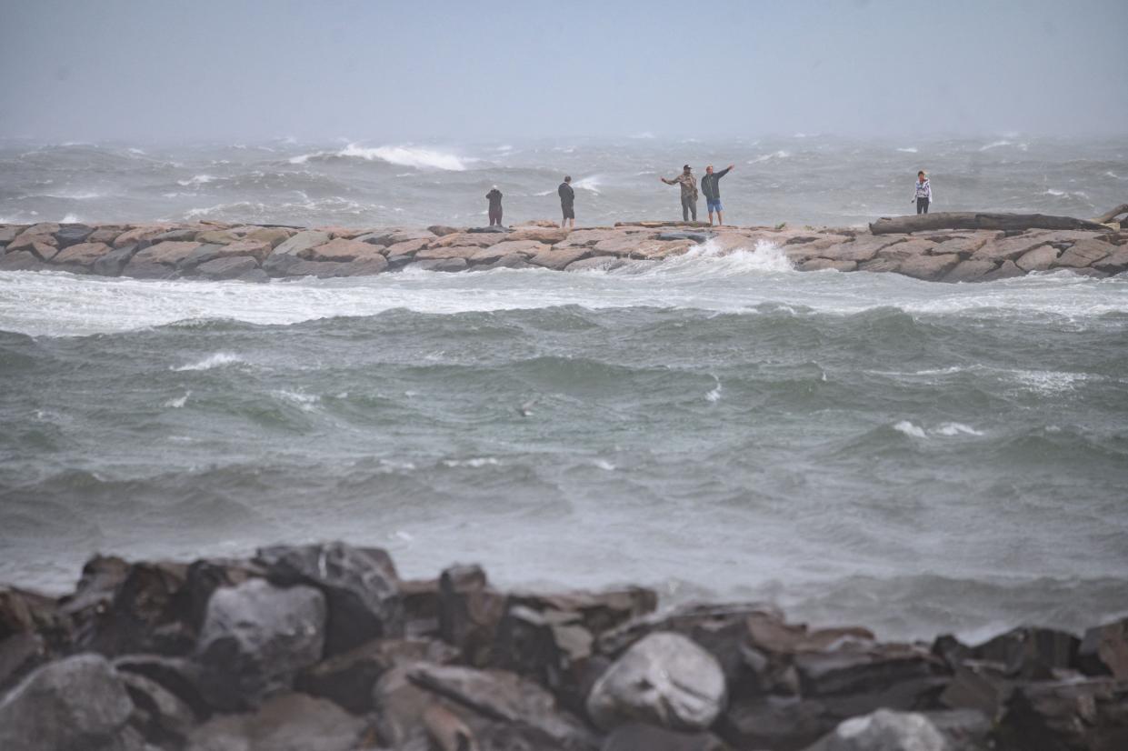 People watch the waves as they stand on a beach as Tropical Storm Henri passes, in Montauk, Long Island on August 22, 2021.