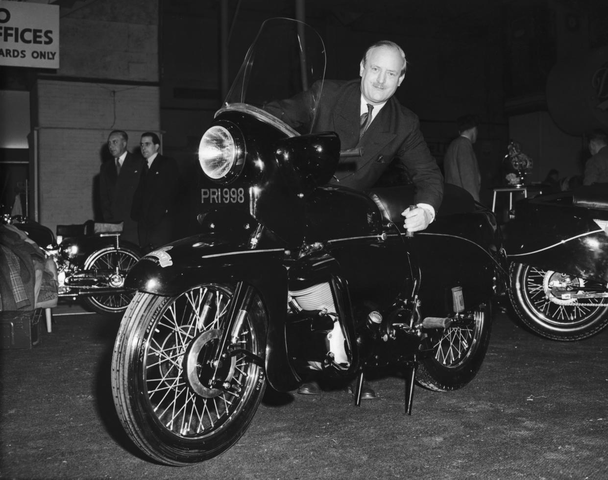 Motorbike designer Philip C. Vincent demonstrates the new rolling centre stand of the Vincent Black Prince at the Cycle and Motorcycle Show at Earl's Court, 12th November 1954. (Photo by L. Blandford/Topical Press Agency/Hulton Archive/Getty Images)