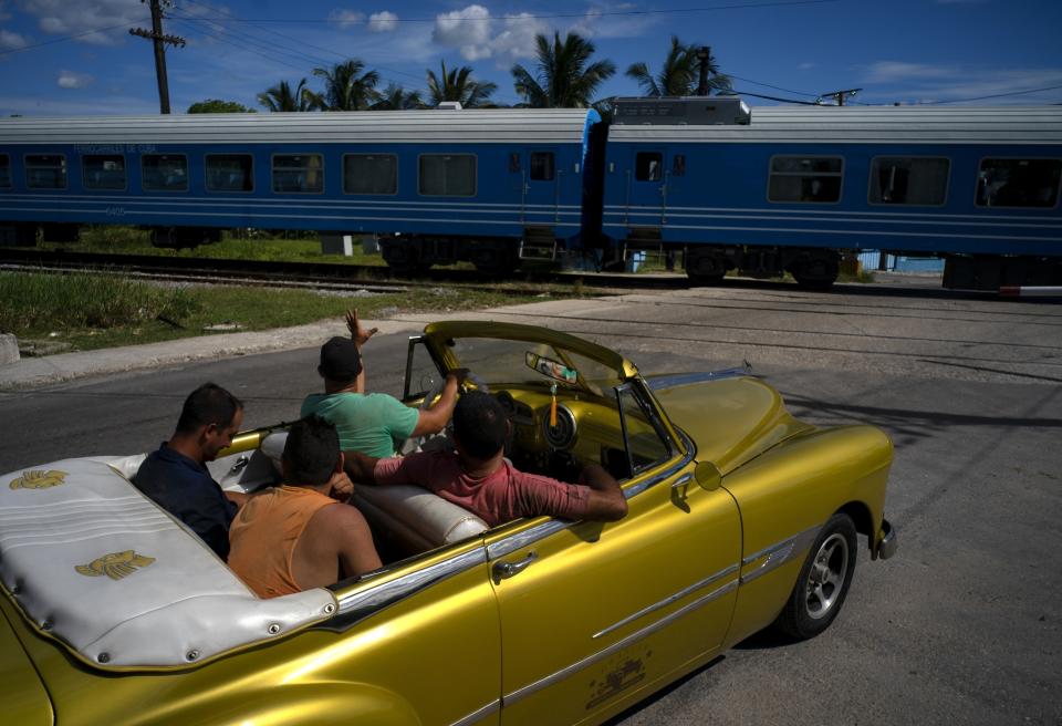 A driver in an American classic car waves as the first train using new equipment from China rides past, in Havana, Cuba, Saturday, July 13, 2019. The first train using new equipment from China pulled out of Havana Saturday, hauling passengers on the start of a 915-kilometer (516-mile) journey to the eastern end of the island as the government tries to overhaul the country’s aging and decrepit rail system. (AP Photo/Ramon Espinosa)