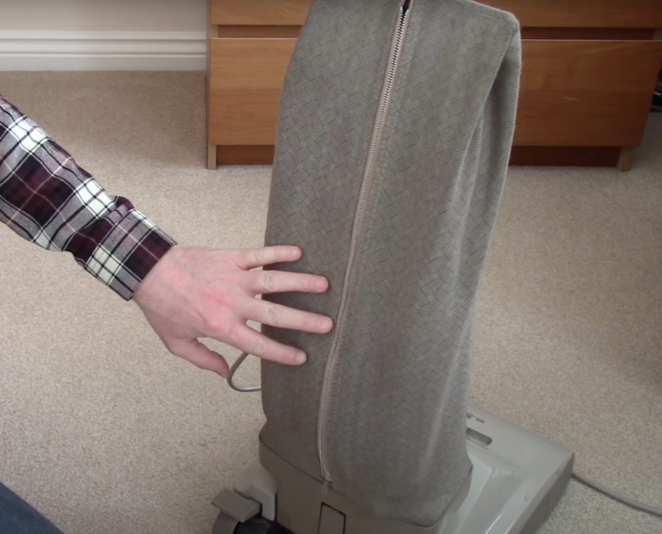 Screen shot of hand touching back of upright vacuum bag