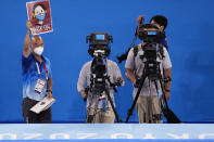 Rich Lam, left, gymnastics photo manager, holds up a sign that signals athletes to put their masks on while standing on the medal podium after the men's artistic gymnastic team competition at the 2020 Summer Olympics, Monday, July 26, 2021, in Tokyo, Japan. (AP Photo/Ashley Landis)