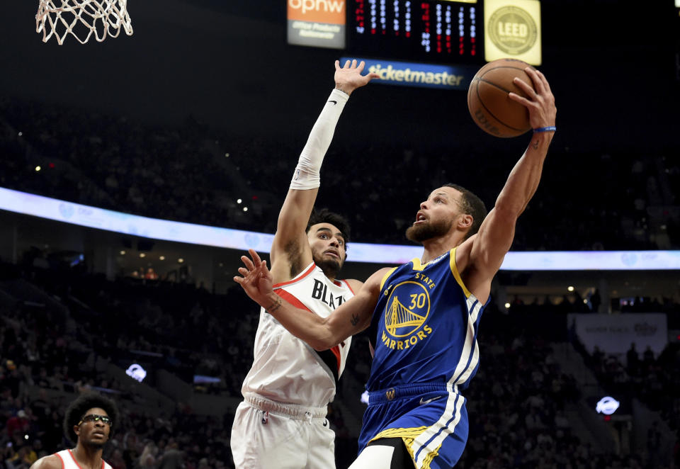 Golden State Warriors guard Stephen Curry, right, drives to the basket against Portland Trail Blazers forward Justin Minaya, center left, during the first half of an NBA basketball game in Portland, Ore., Thursday, April 11, 2024. (AP Photo/Steve Dykes)