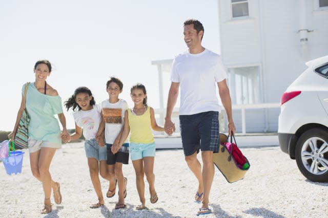 Family holding hands and walking with beach gear in sunny driveway