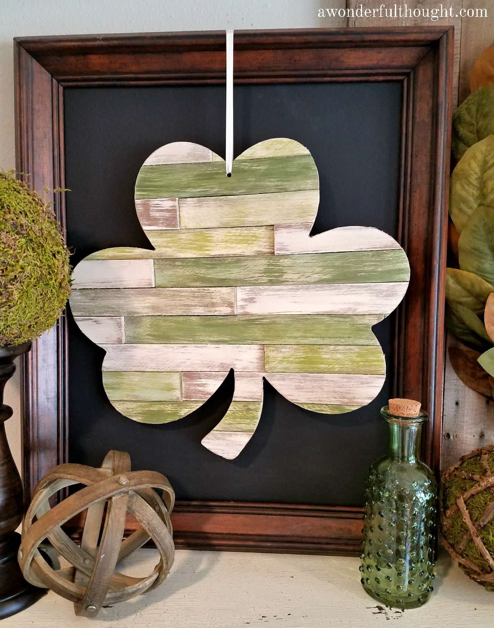 a shamrock made out of wood shims framed and sitting on a shelf with a green bottle
