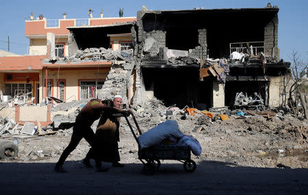 Men push a cart in front of a building destroyed during clashes between Iraqi forces and Islamic State fighters in Mosul, Iraq November 24, 2016. REUTERS/Goran Tomasevic