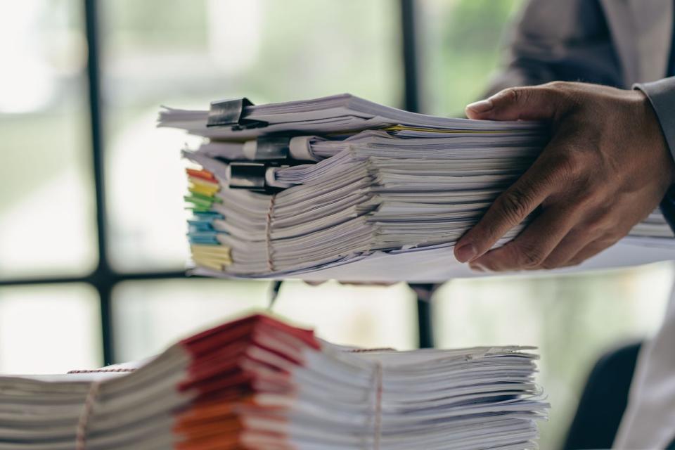 A person holds a large stack of documents.