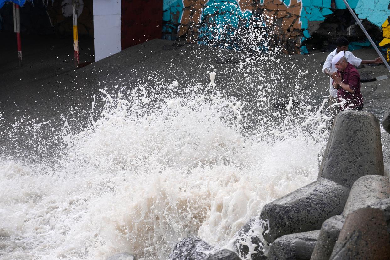 A man, right, performs rituals as waves hit the shore during high tide on the Arabian Sea coast in Mumbai (AP)