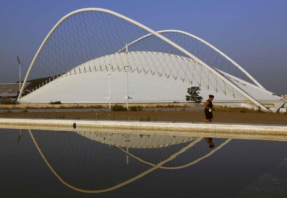 A woman jogs past the Velodrome at the Athens 2004 Olympic Complex in Athens July 27, 2014. Ten years after Greece hosted the world's greatest sporting extravaganza, many of its once-gleaming Olympic venues have been abandoned while others are used occasionally for non-sporting events such as conferences and weddings. For many Greeks who swelled with pride at the time, the Olympics are now a source of anger as the country struggles through a six-year depression, record unemployment, homelessness and poverty. Just days before the anniversary of the Aug. 13-29 Games in 2004, many question how Greece, among the smallest countries to ever host the Games, has benefited from the multi-billion dollar event. Picture taken July 27, 2014. REUTERS/Yannis Behrakis (GREECE - Tags: BUSINESS POLITICS SOCIETY SPORT TPX IMAGES OF THE DAY) ATTENTION EDITORS: PICTURE 03 OF 33 FOR WIDER IMAGE PACKAGE 'TEN YEARS ON - ATHENS' FADING OLYMPIC STADIUMS' TO FIND ALL IMAGES SEARCH 'BEHRAKIS KARAHALIS'