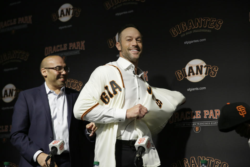 San Francisco Giants manager Gabe Kapler tries on his new jersey after being introduced by president of baseball operations Farhan Zaidi, left, during a news conference at Oracle Park Wednesday, Nov. 13, 2019, in San Francisco. Kapler has been hired as manager of the San Francisco Giants, a month after being fired from the same job by the Philadelphia Phillies. Kapler replaces Bruce Bochy, who retired at the end of the season following 13 years and three championships with San Francisco. (AP Photo/Eric Risberg)