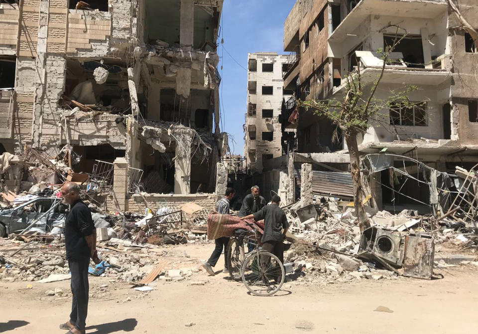 FILE - People stand in front of damaged buildings, in the town of Douma, the site of a suspected chemical weapons attack, near Damascus, Syria, Monday, April 16, 2018. A report published Friday, Jan. 27, 2023, by a team from the Organization for the Prohibition of Chemical Weapons established there are “reasonable grounds to believe” Syria's air force dropped two cylinders containing chlorine gas on the city of Douma in April 2018, killing 43 people. (AP Photo/Hassan Ammar, File)