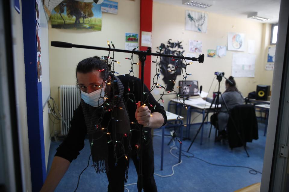 Music teacher, Nikos Karadosidis, uses Christmas lights as a makeshift "recording" light, warning those outside the classroom to be quiet during recording sessions at Avlona's prison school, north of Athens, Wednesday, Feb. 10, 2021. With Greece's schools shut due to the pandemic, all lessons have gone online. But the online world isn't within reach of everyone _ and particularly not within reach of the students of Avlona Special Youth Detention Center, where internet devices are banned by law from the cells. (AP Photo/Thanassis Stavrakis)