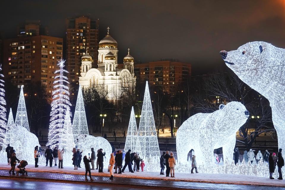 People walk and play at a park decorated for the New Year and Christmas festivities with an Orthodox Church in the background in Moscow, Russia, Sunday, Dec. 24, 2023. (AP Photo/Alexander Zemlianichenko)