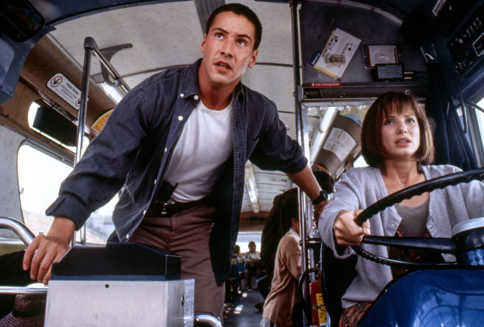 Keanu's character looks on as Sandra's character drives the bus