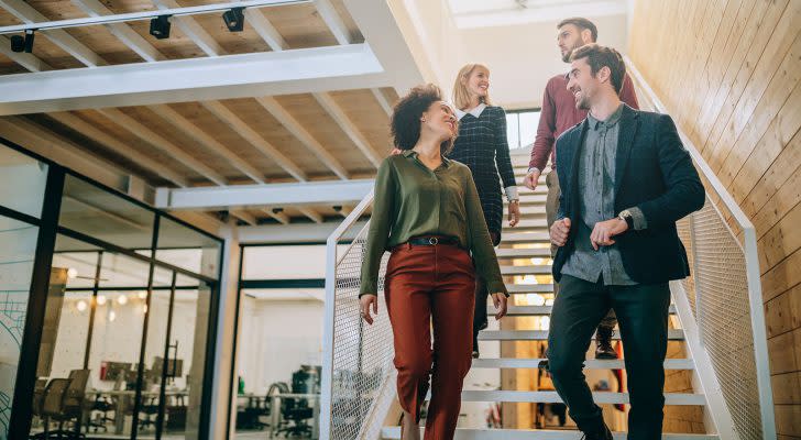 A group of four coworkers walking down the stairs in their office building.