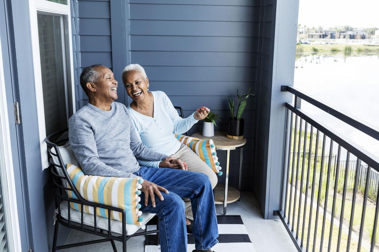 A senior African-American couple sitting side by side on their porch or balcony, relaxing, and holding hands, conversing and laughing together