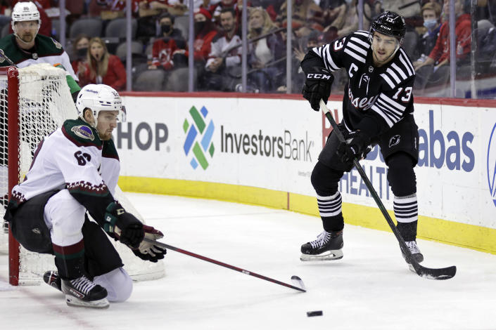 New Jersey Devils center Nico Hischier (13) passes around Arizona Coyotes defenseman Janis Moser during the first period of an NHL hockey game Wednesday, Jan. 19, 2022, in Newark, N.J. (AP Photo/Adam Hunger)