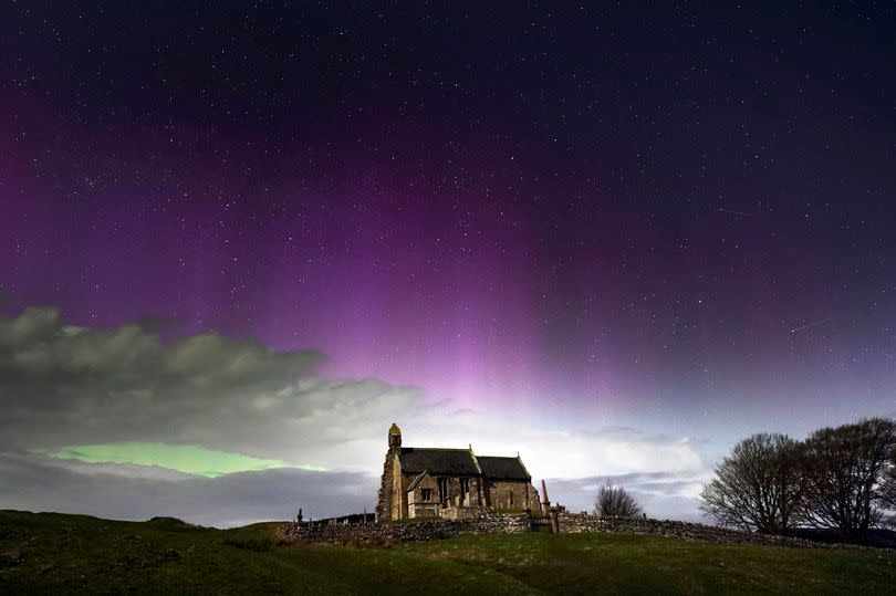 The aurora borealis, also known as the Northern Lights, illuminate the sky just before midnight over St Aidan's church in Thockrington, Northumberland on Tuesday, April 16