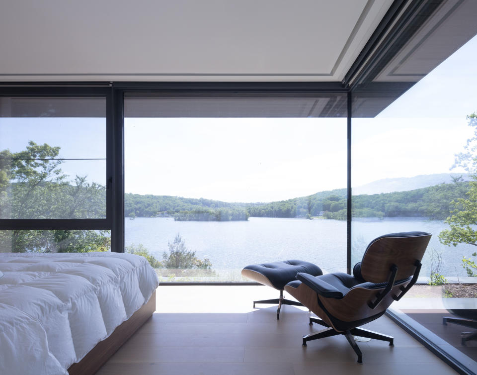 A minimalist bedroom with leather lounge chair a large windows with panoramic lake views