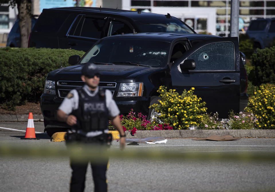 A police officer standing near a windshield and passenger window of an RCMP vehicle with bullet holes at the scene of a shooting in Langley, British Columbia, Monday, July 25, 2022. (Darryl Dyck/The Canadian Press via AP)