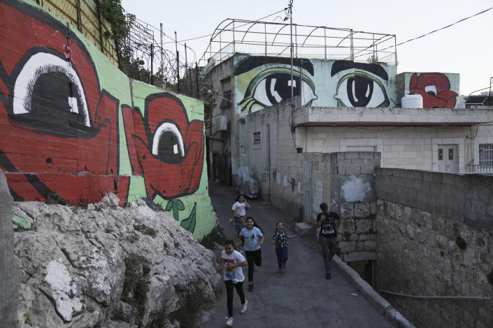 Palestinian children walk between murals that are part of the public art project 'I Witness Silwan', in the Silwan neighbourhood of east Jerusalem, Friday, Aug. 26, 2022. At right are the eyes of Silwan Community Member Nihad Siyam; at left, eyes inside two poppies, which Palestinians call their national flower. Eyes are always open in this flashpoint district. Now, new eyes emerged; they were painted on the walls of the decaying Palestinian homes. The eye murals, and graffiti of Palestinian symbols, are so giant that make you feel they are watching you wherever you walk in the neighborhood. (AP Photo/ Mahmoud Illean)